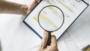 Mão segurando lupa faz análise de contrato, simbolizando os cuidados ao comprar um imóvel.