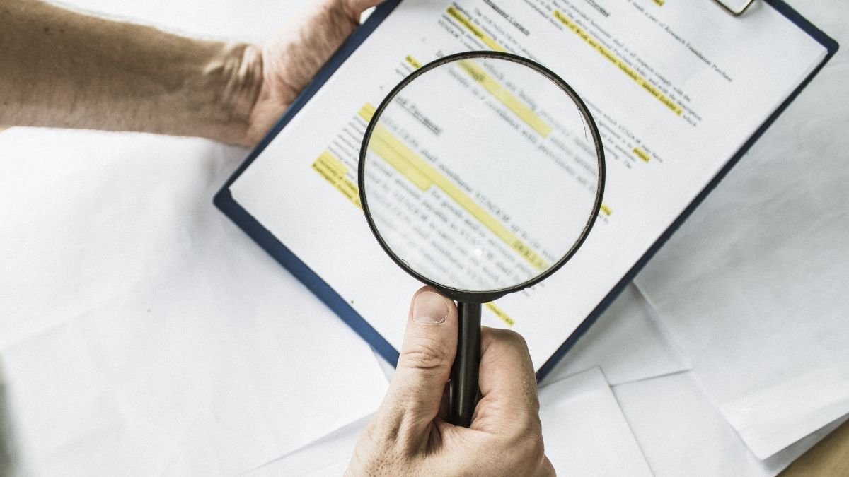 Mão segurando lupa faz análise de contrato, simbolizando os cuidados ao comprar um imóvel.